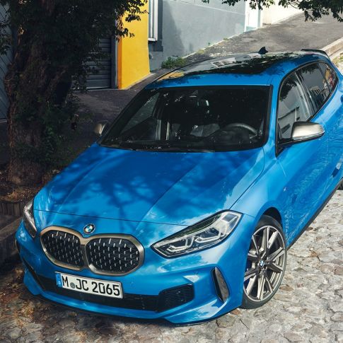 1 Series BMW at the roadside. 1 Series BMW in Misano Blue metallic, three-quarter front view, parking at the roadside from a bird’s eye view.