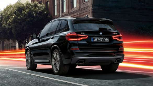 BMW X3 M40i SUV G01, three-quarter rear view. BMW X3 M40i SUV G01 in Black Sapphire metallic, driving, exterior, three-quarter rear view before an urban background with light strips.
