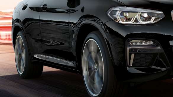 BMW X4 M40i and BMW X4 M40d SUV G02, three-quarter side view. BMW X4 M40i and BMW X4 M40d SUV G02 in Black Sapphire metallic, driving, exterior, three-quarter side view with rotating light alloy wheels.