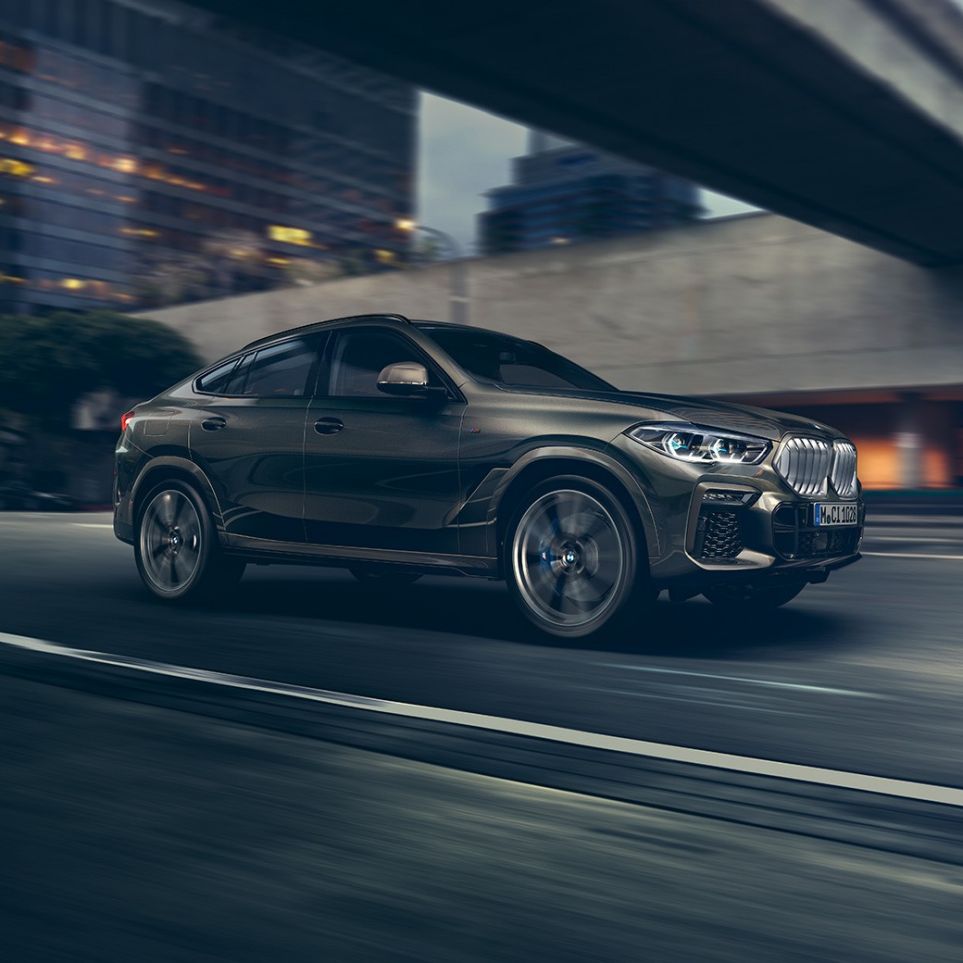 BMW X6 SUV G06 driving. BMW X6 SUV G06 in three-quarter front perspective driving in front of an urban setting.