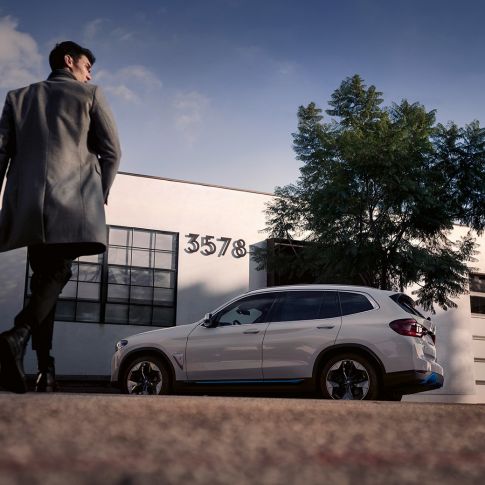 BMW iX3 SUV G08 side view in front of building with man BMW iX3 SUV G08 2020 Mineral White metallic side view in front of building with man