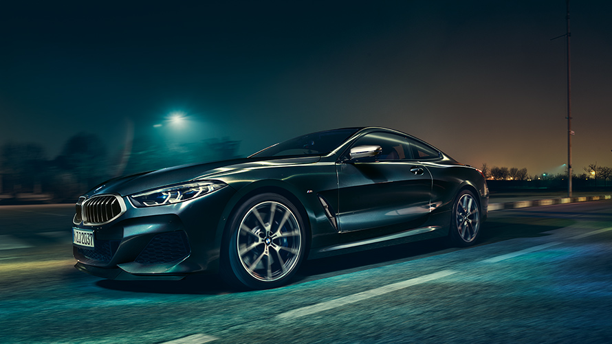 A three-quarter front still shot of the BMW 8 Series Coupé in an urban setting at night.
