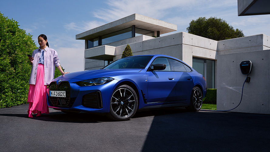 BMW i4 M50 G26 2021 BMW Individual Frozen Portimao Blue metallic three-quarter side view with woman in front of house