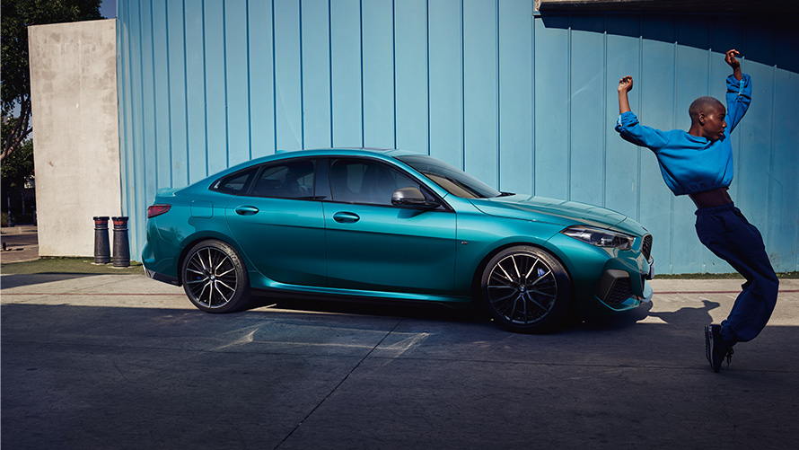 BMW M235i xDrive Gran Coupé F44 side view with woman in the front BMW M235i xDrive Gran Coupé F44 Snapper Rocks Blue metallic side view with woman in the front