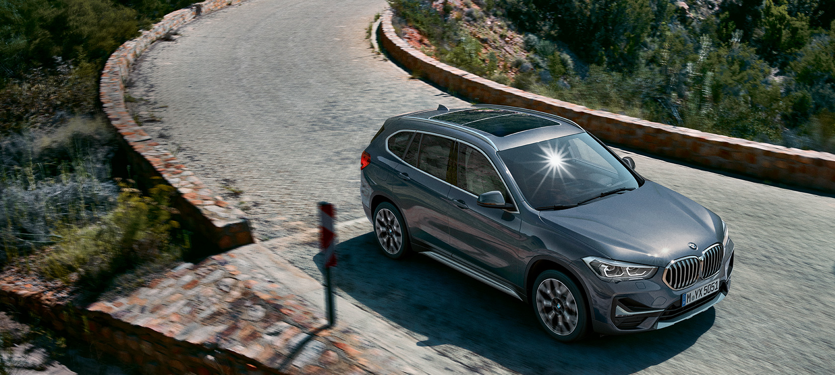 BMW X1 SUV F48, three-quarter front view. BMW X1 SUV F48, three-quarter front view driving in front of mountain scenery.