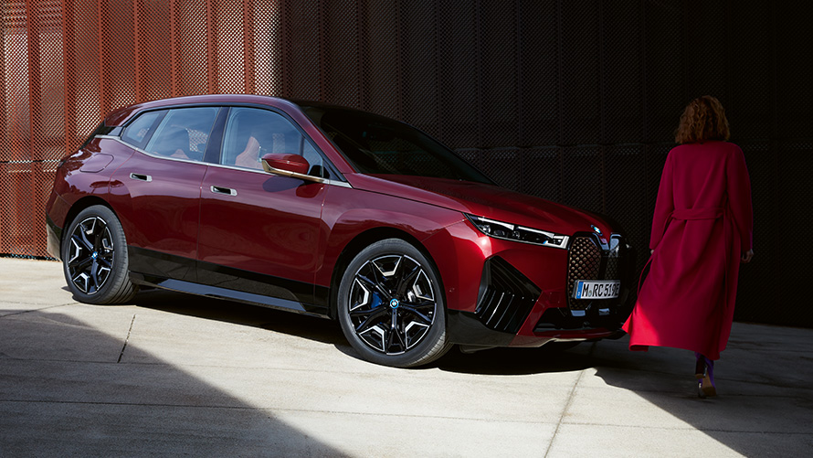 Woman in front of BMW iX i20 2021 three quarter front view Woman in red coat in front of BMW iX i20 2021 three quarter front view