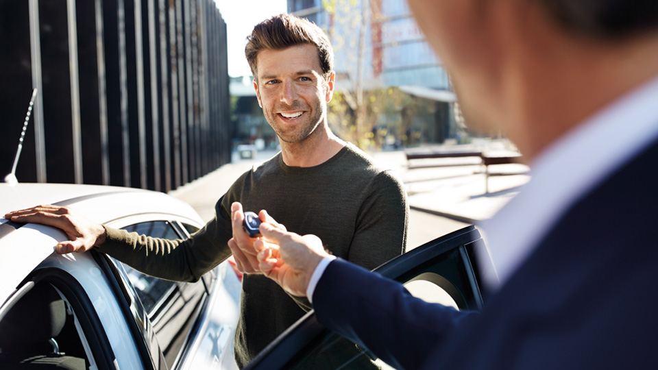 Man stands at the open driver's door and hands over the vehicle key to the BMW customer advisor