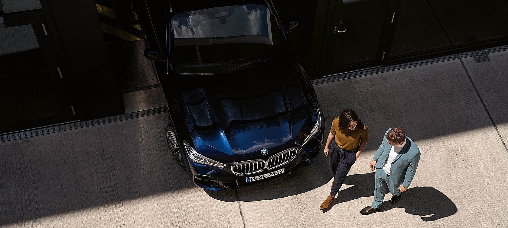 Woman and man walk past the front of the BMW Woman and man walk past the front of a BMW from bird's eye view